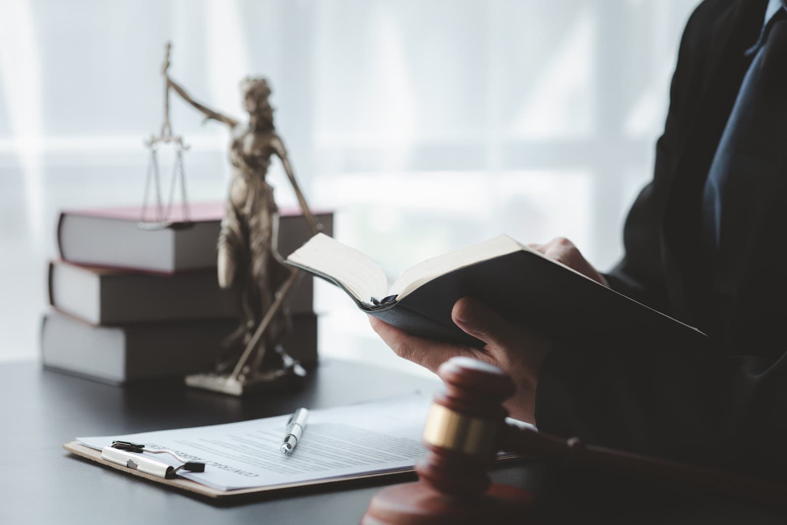 Livro de leis aberto ao lado da estatua da Justica.