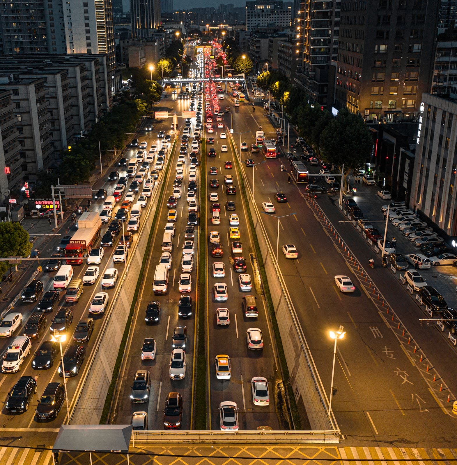 Tráfego urbano noturno com carros em avenida iluminada da cidade.