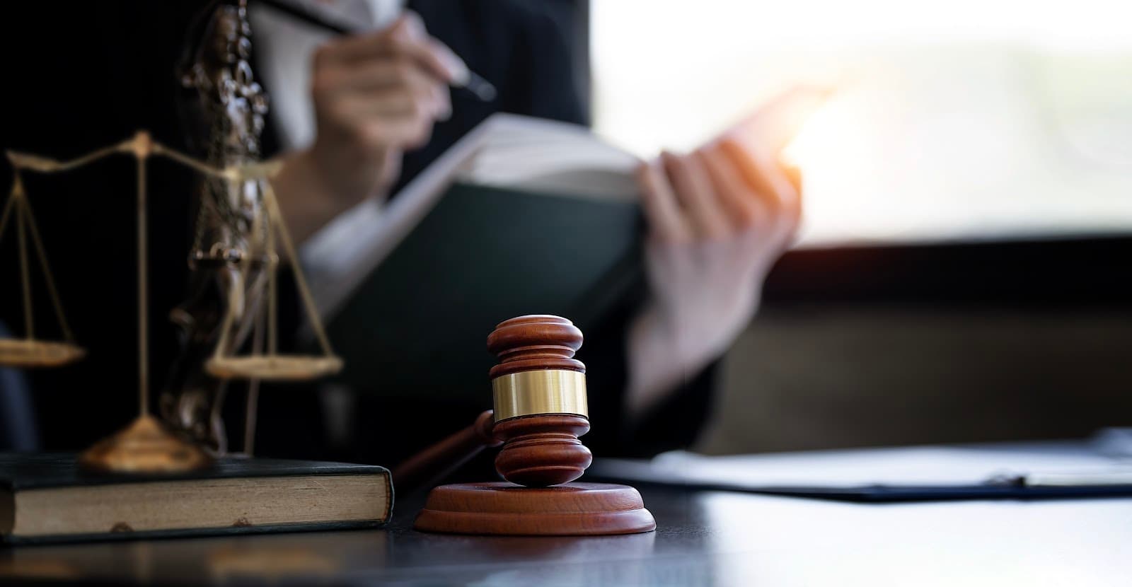Martelo de juiz, livros de leis e balança da justiça sobre uma mesa de madeira.