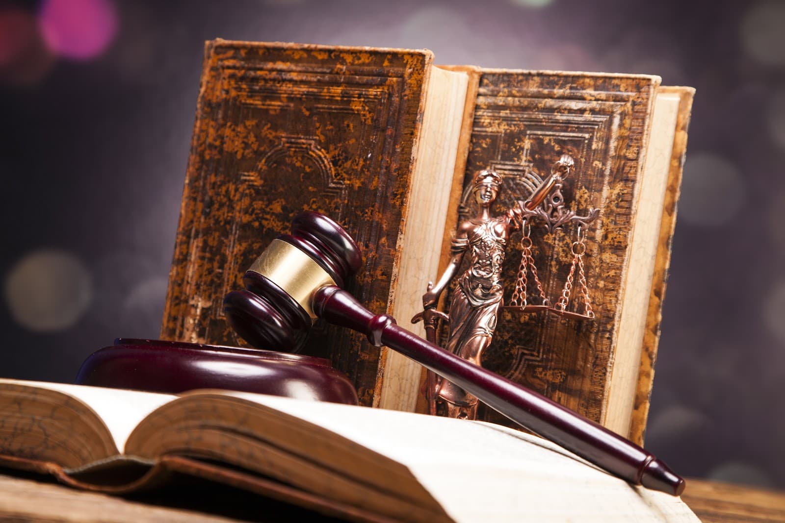 Livros de leis, estatueta da Justiça e um martelo sobre uma mesa de madeira.