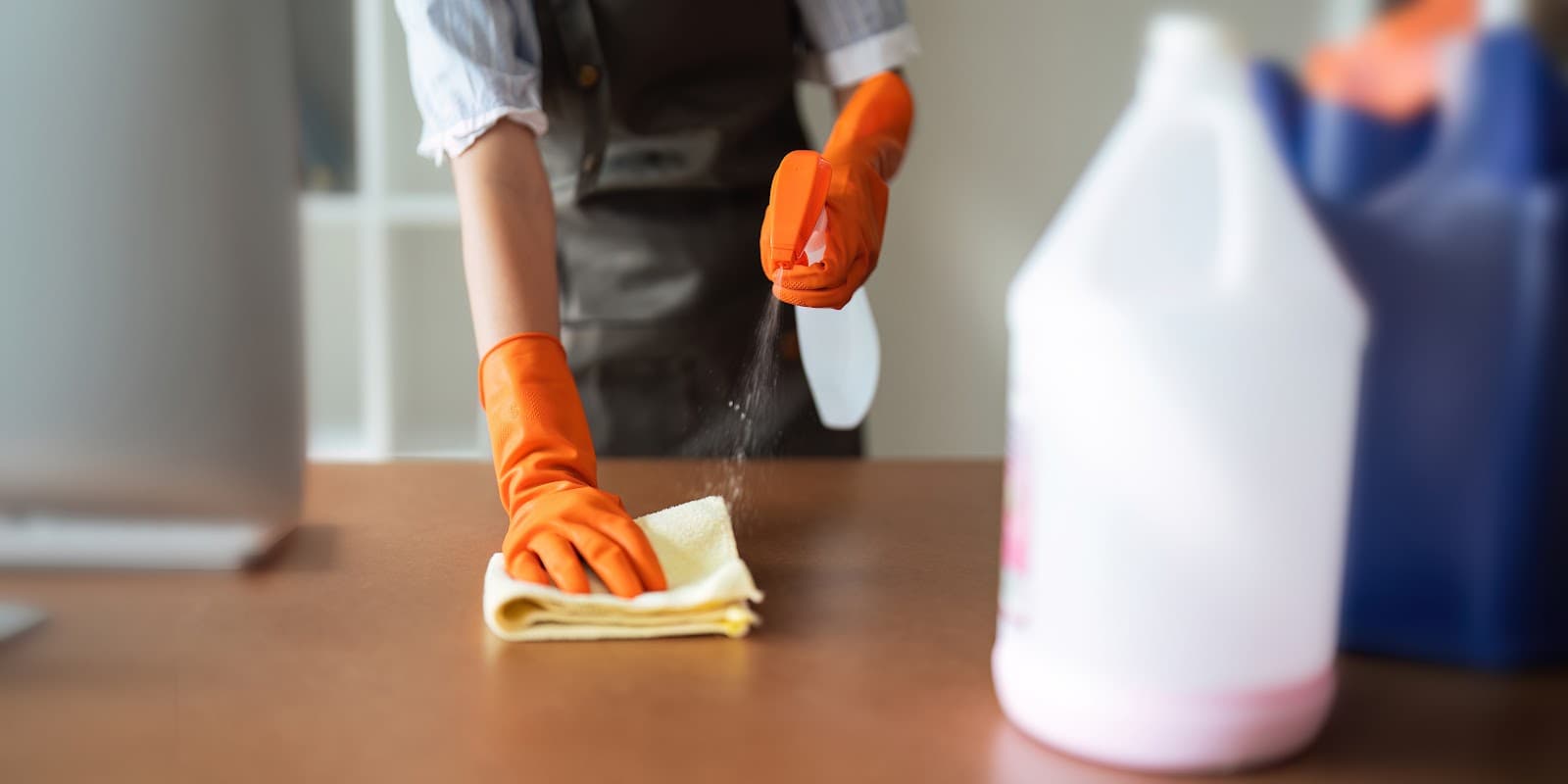 Profissional de limpeza utilizando borrifador e pano para desinfetar superficie em ambiente escolar.