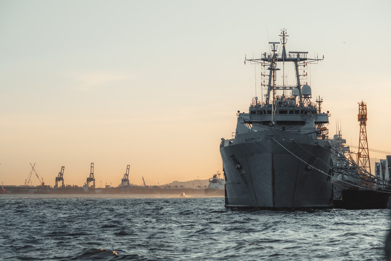 Grande navio industrial atracado em um porto durante o pôr do sol.