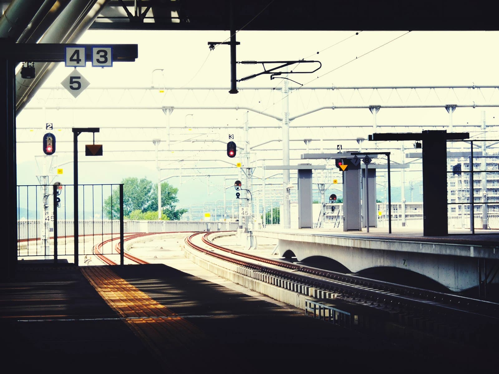 Plataforma de estação de transporte público com trilhos e cobertura metálica.