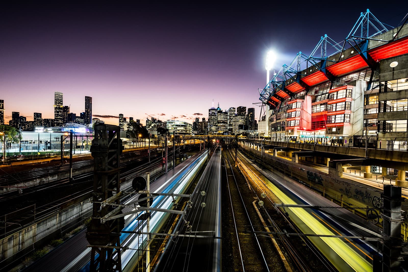 Imagem ilustrativa: exterior de estádio iluminado, com trilhos em primeiro plano.