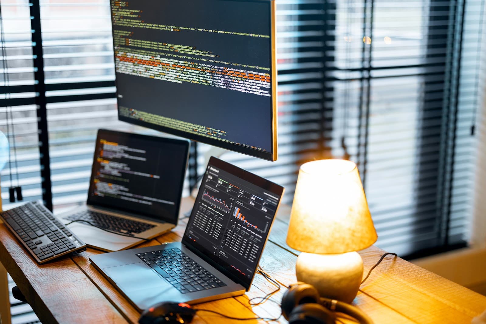 Mesa de trabalho com dois notebooks e monitor iluminados