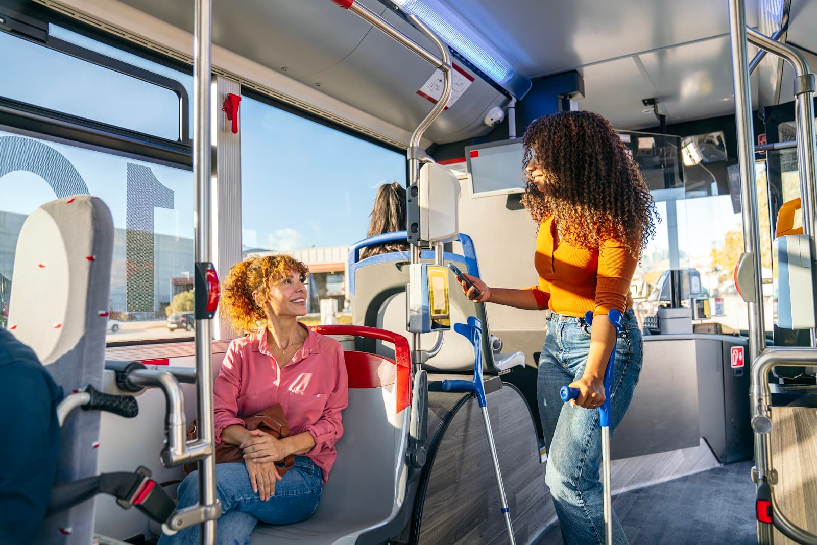 Duas mulheres conversam sentadas em um ônibus em movimento durante o dia