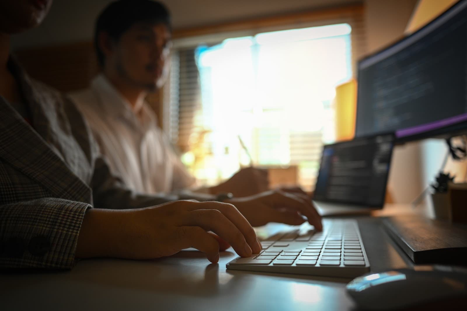 Profissionais digitando em teclados de computadores em ambiente corporativo moderno.